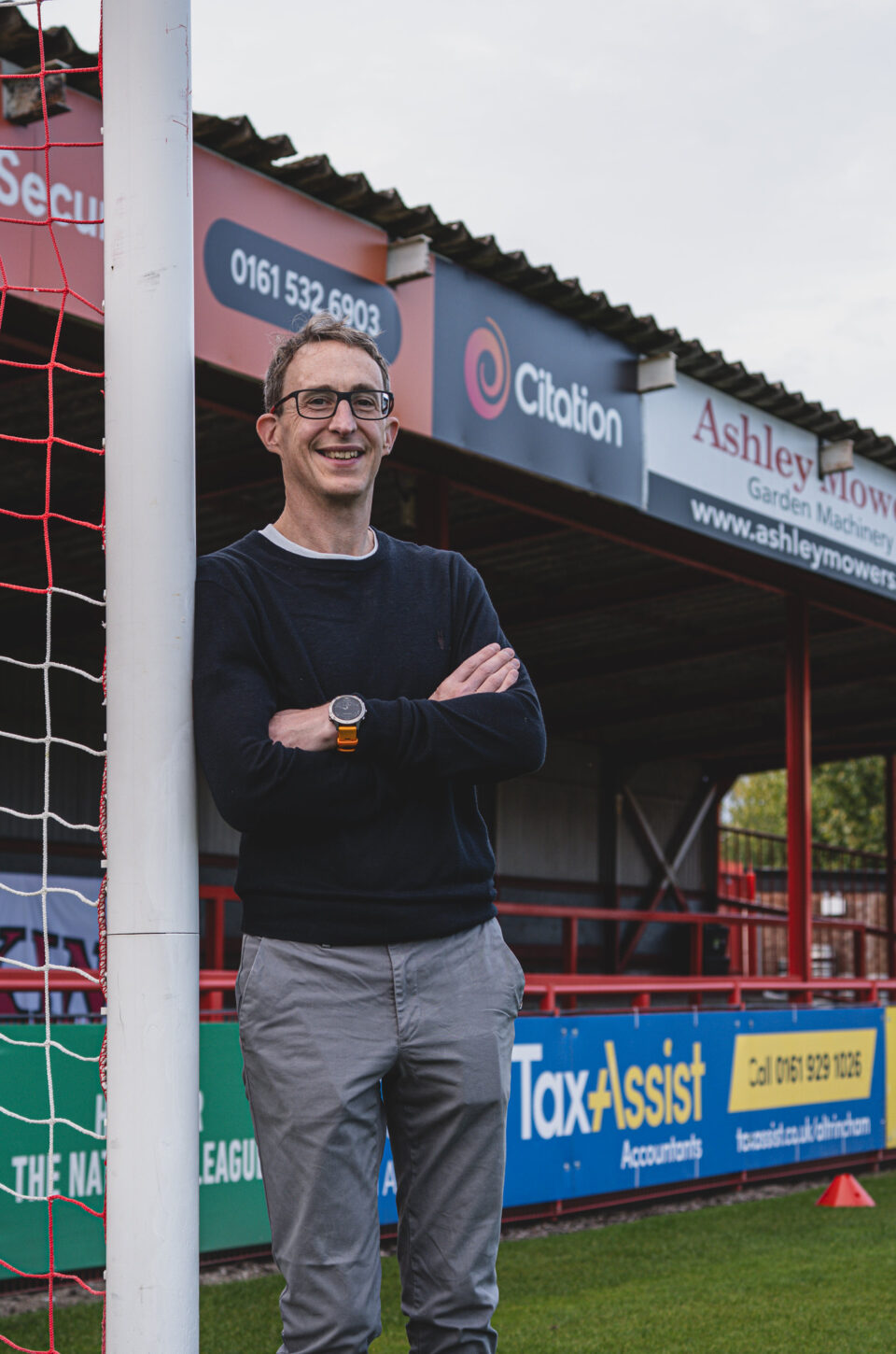 Matt Stewart, Citation's managing director, standing in front of Altrincham FC's Golf Road End terrace at the J. Davidson Stadium, showing Citation's new sponsorship branding.